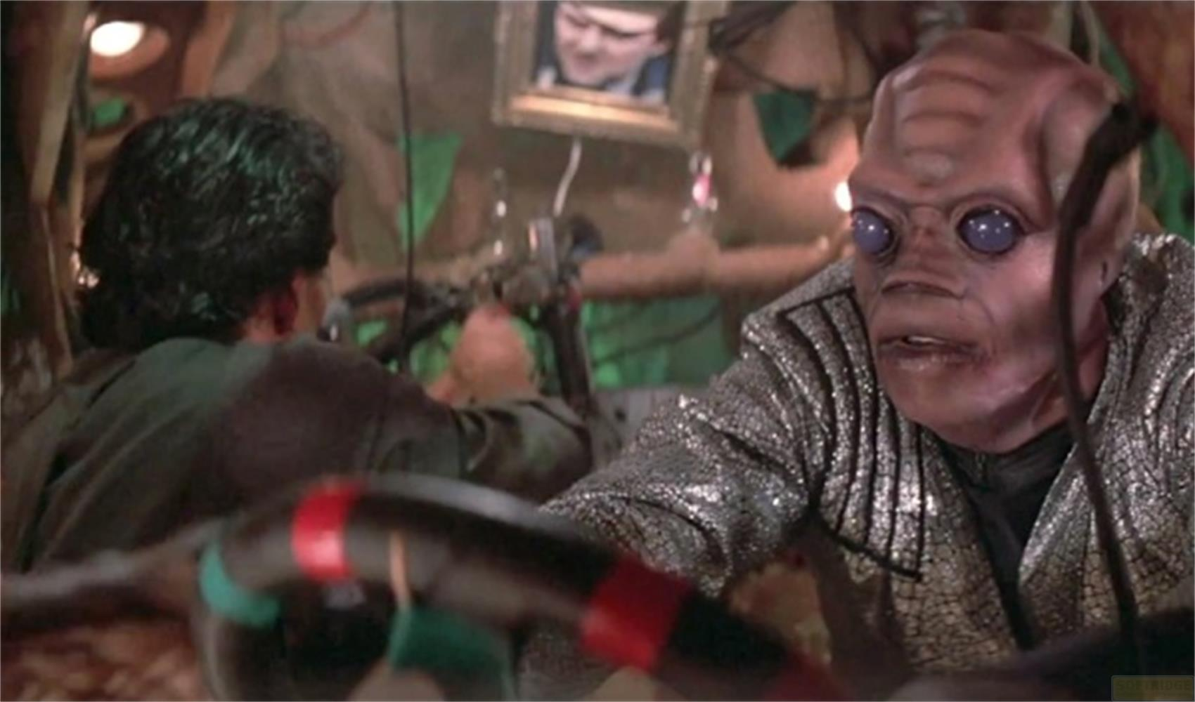 Un alien humanoïde aux yeux bleus porte une veste scintillante.