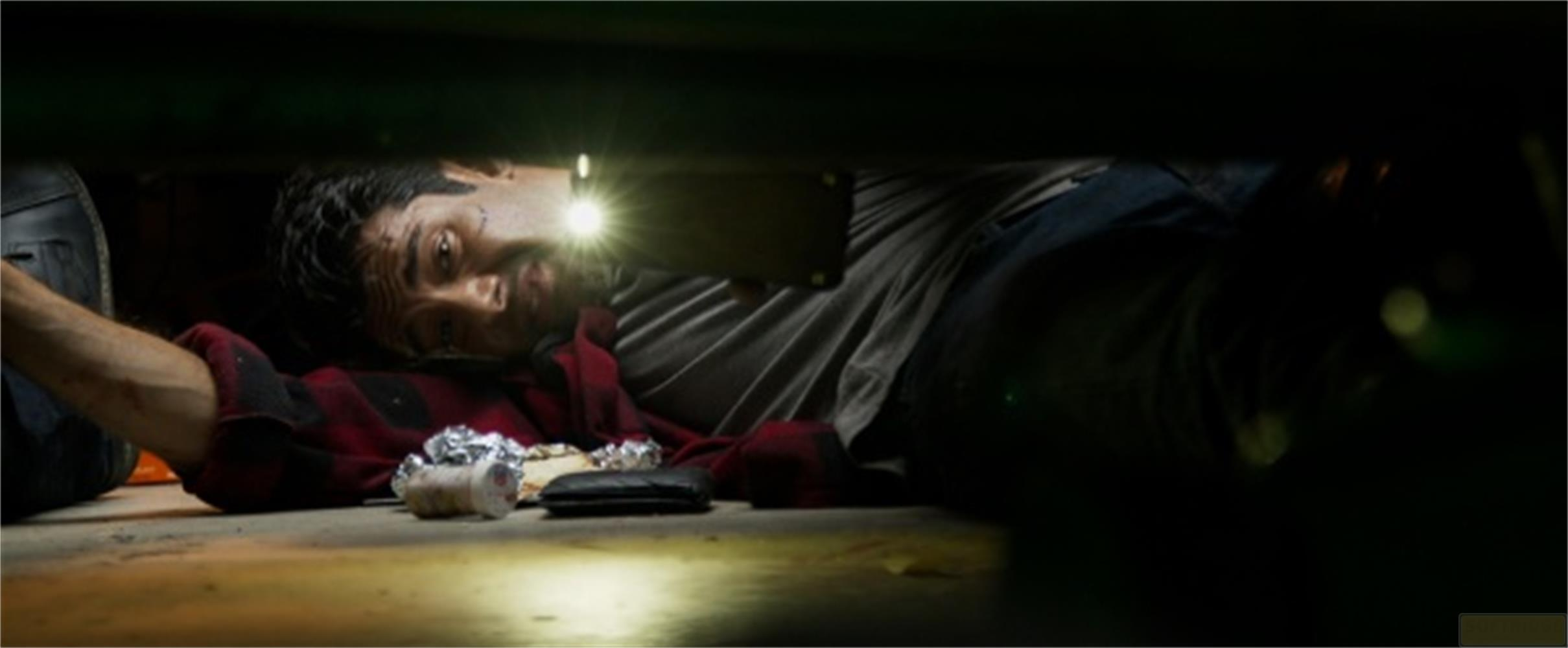 Uomo sdraiato sotto un'auto, si illumina il viso con torcia.