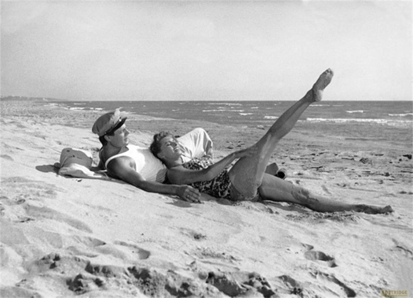 Un uomo e una donna sdraiati su una spiaggia sabbiosa. La donna ha una gamba sollevata.