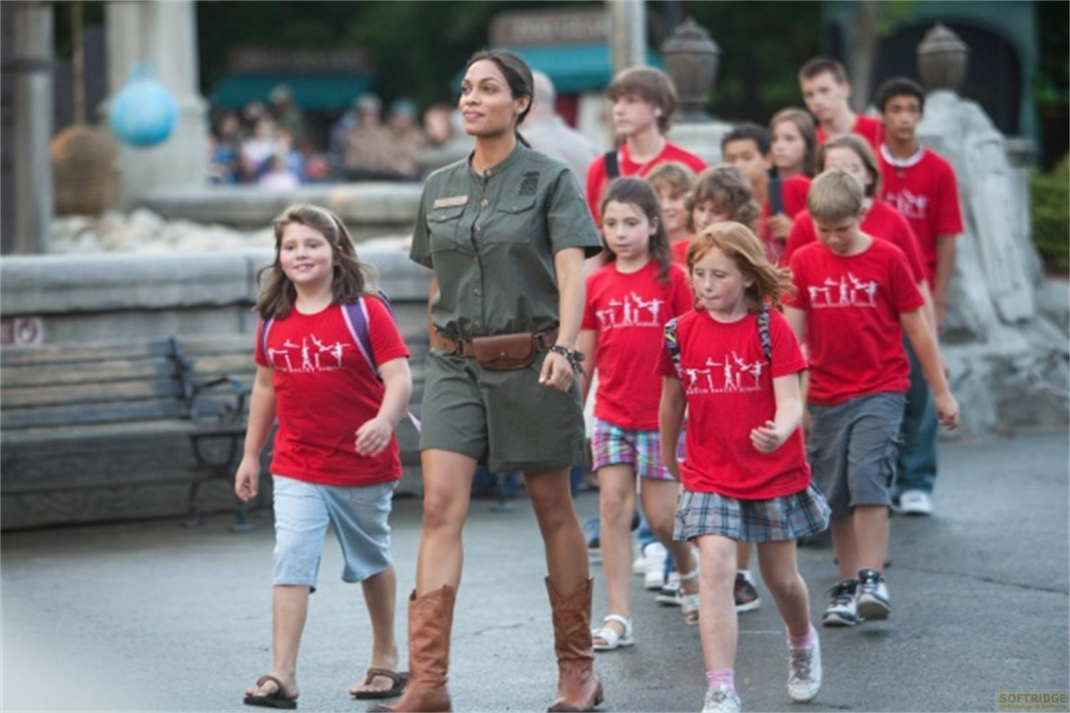 Une femme en uniforme dirige un groupe d'enfants en t-shirts rouges.