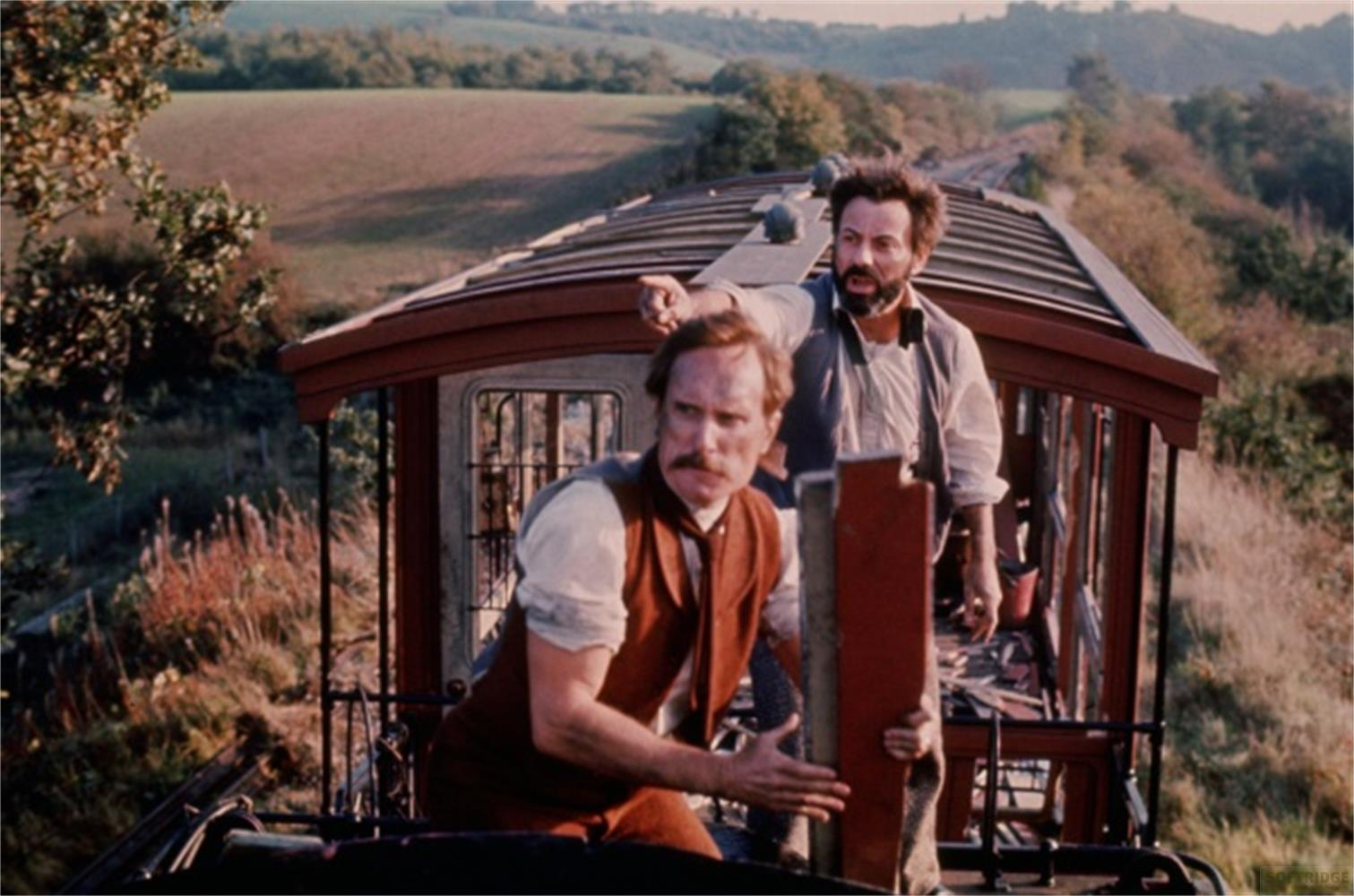 Due uomini sul tetto di un treno di fronte a un paesaggio.