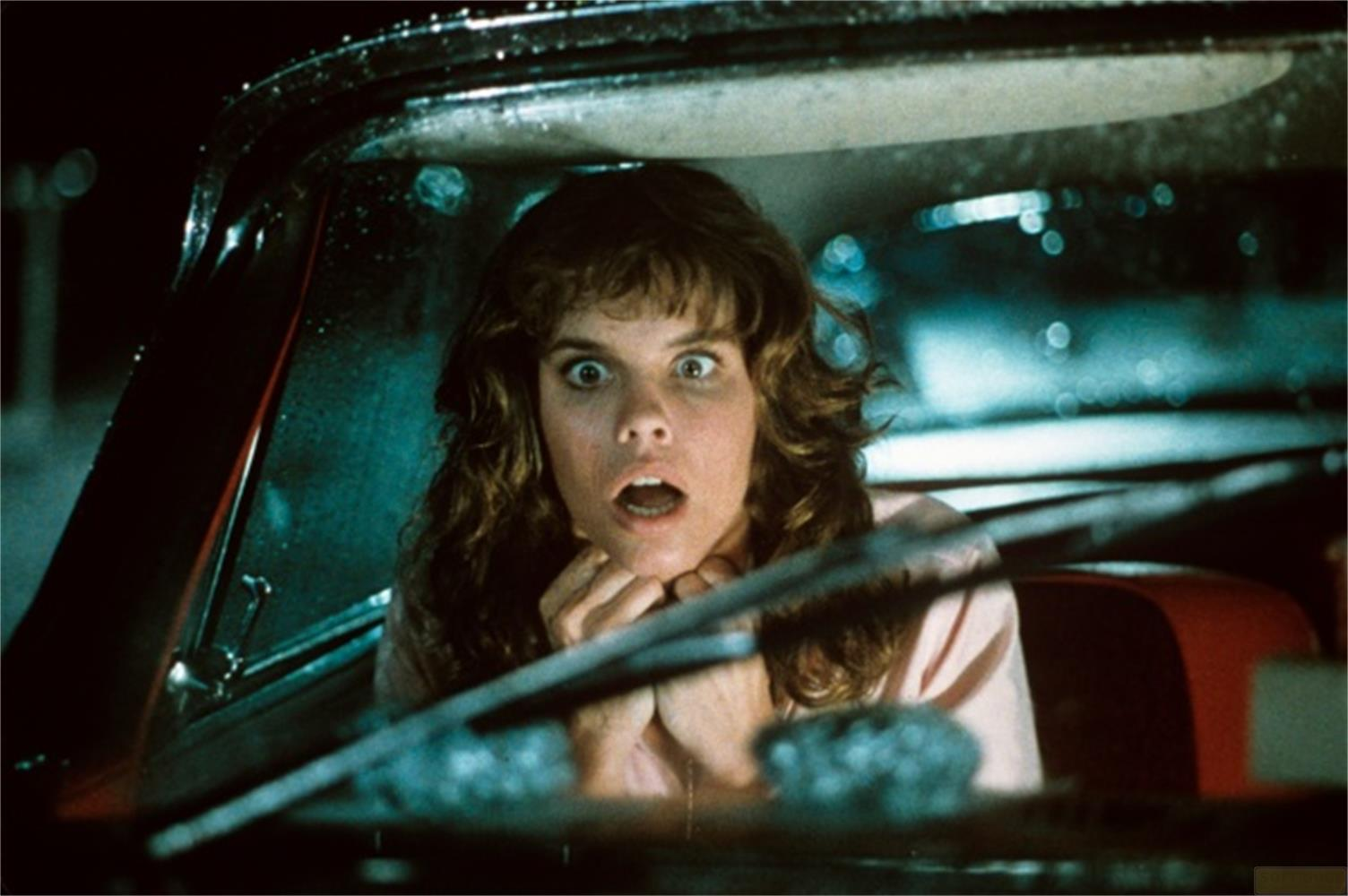 Une femme aux yeux écarquillés regarde hors d'une voiture, l'air choqué.