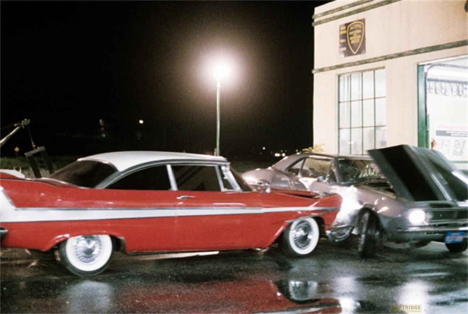 Deux voitures, une rouge et blanche, l'autre argentée, sont la nuit sur une route mouillée.