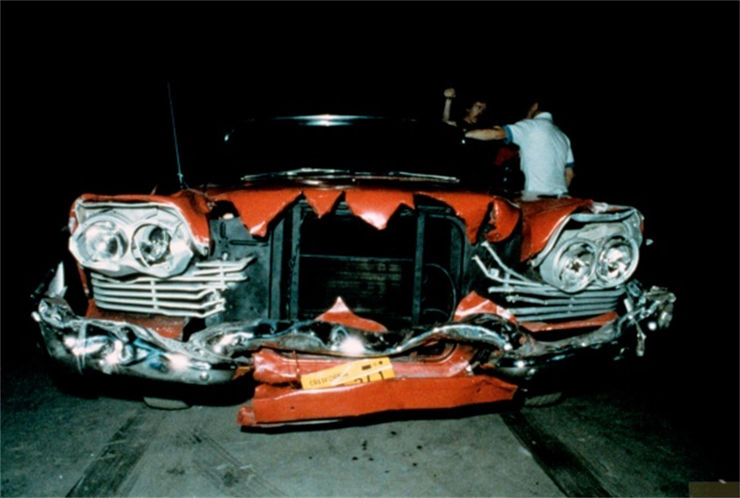 Une voiture rouge au pare-chocs avant très endommagé, deux personnes à l'intérieur.