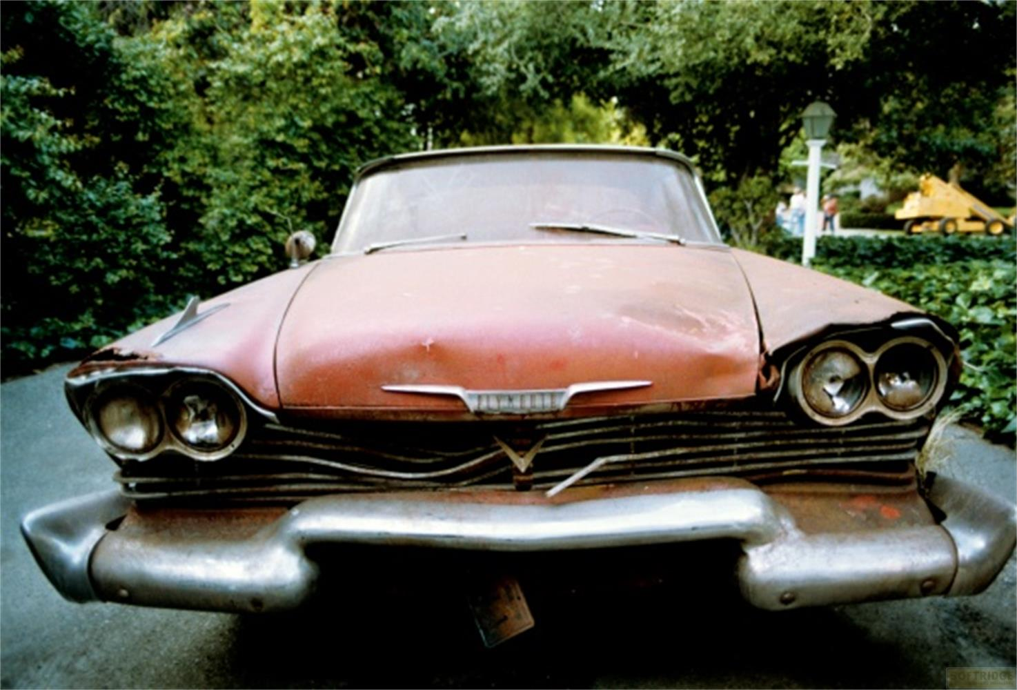 Une voiture ancienne rouge et rouillée avec double phare et calandre chromée.