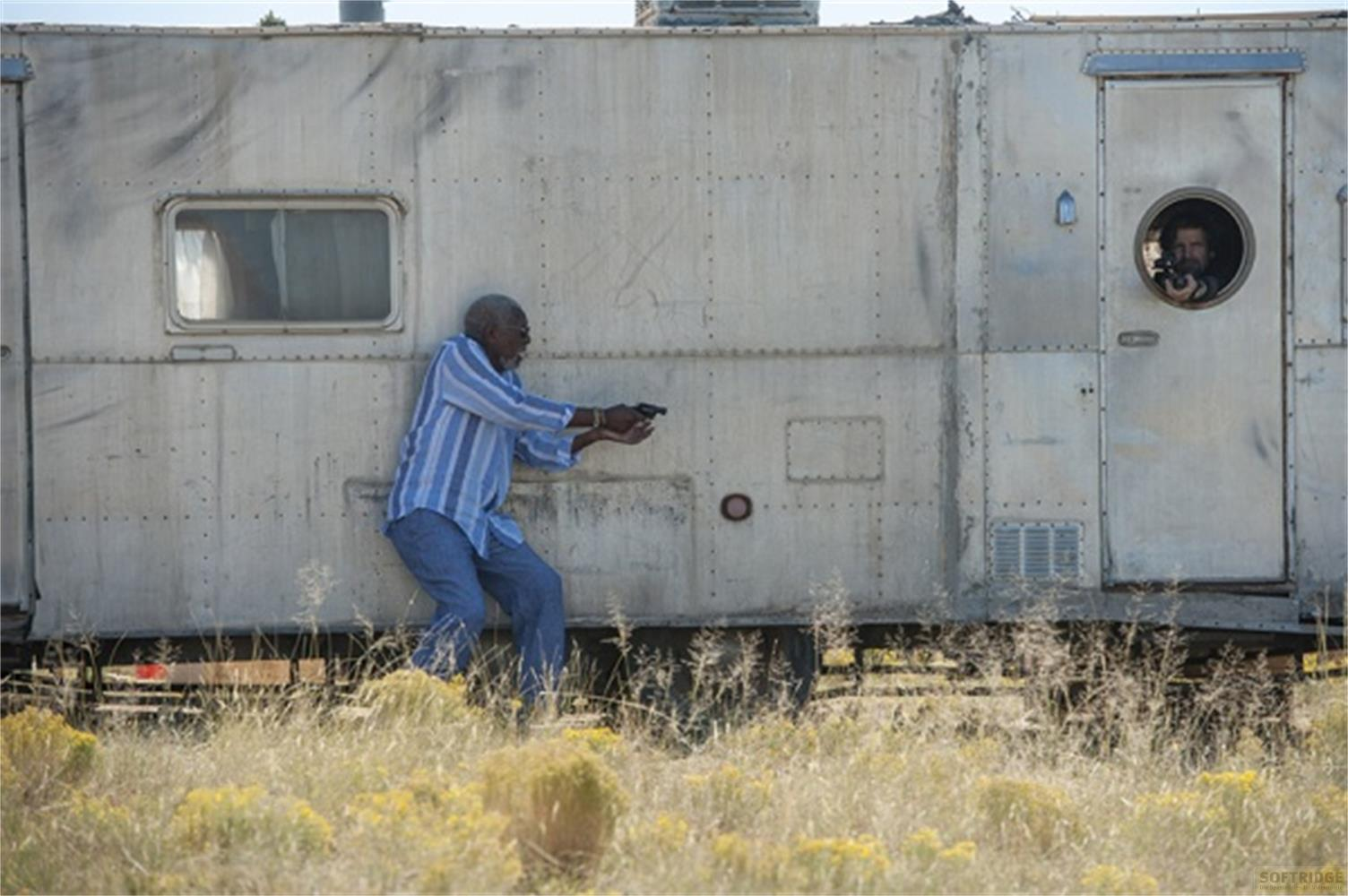 Uomo in camicia a righe tiene pistola fuori dal rimorchio; uomo guarda da finestra rotonda.