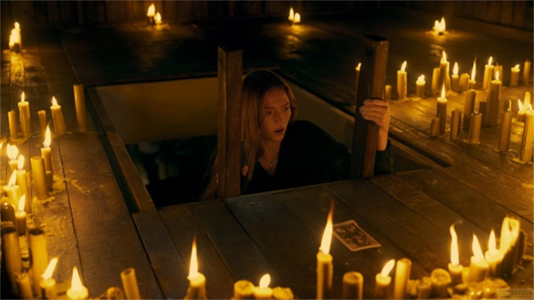 Una donna guarda spaventata in una stanza piena di candele accese su pavimento in legno.