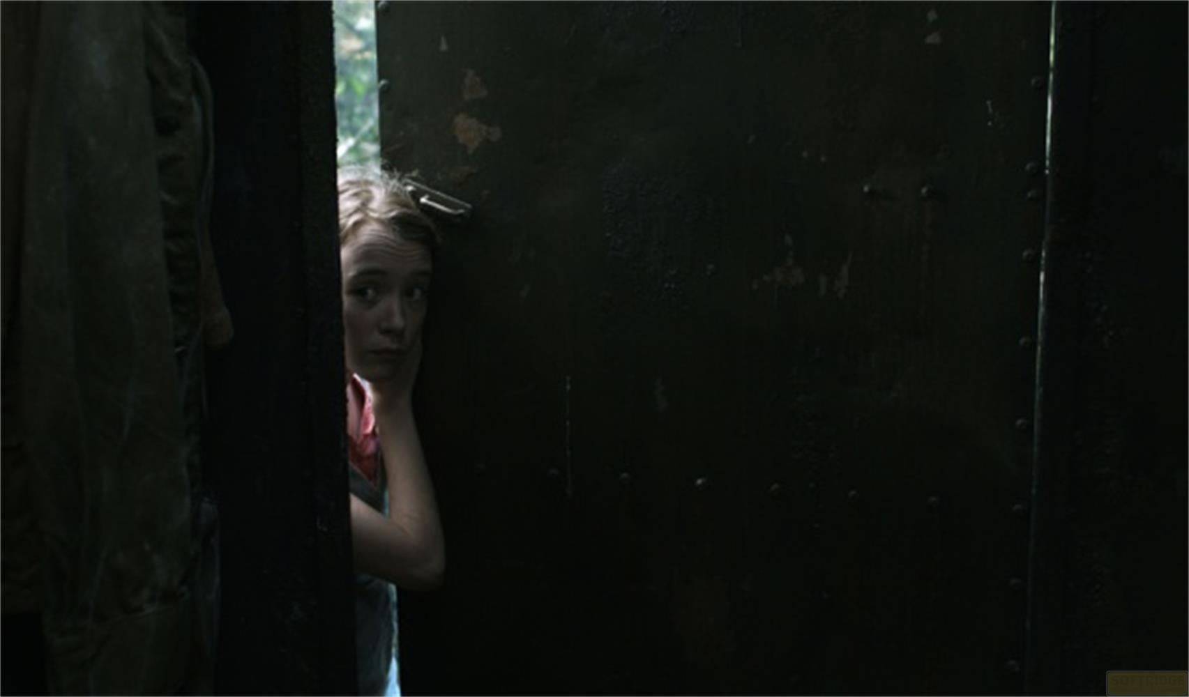 Une fille regarde par une porte sombre. De la verdure est visible dehors.