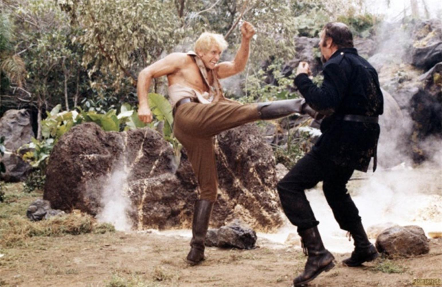 Due uomini combattono in un'area rocciosa e boscosa. Uno calcia con la gamba.
