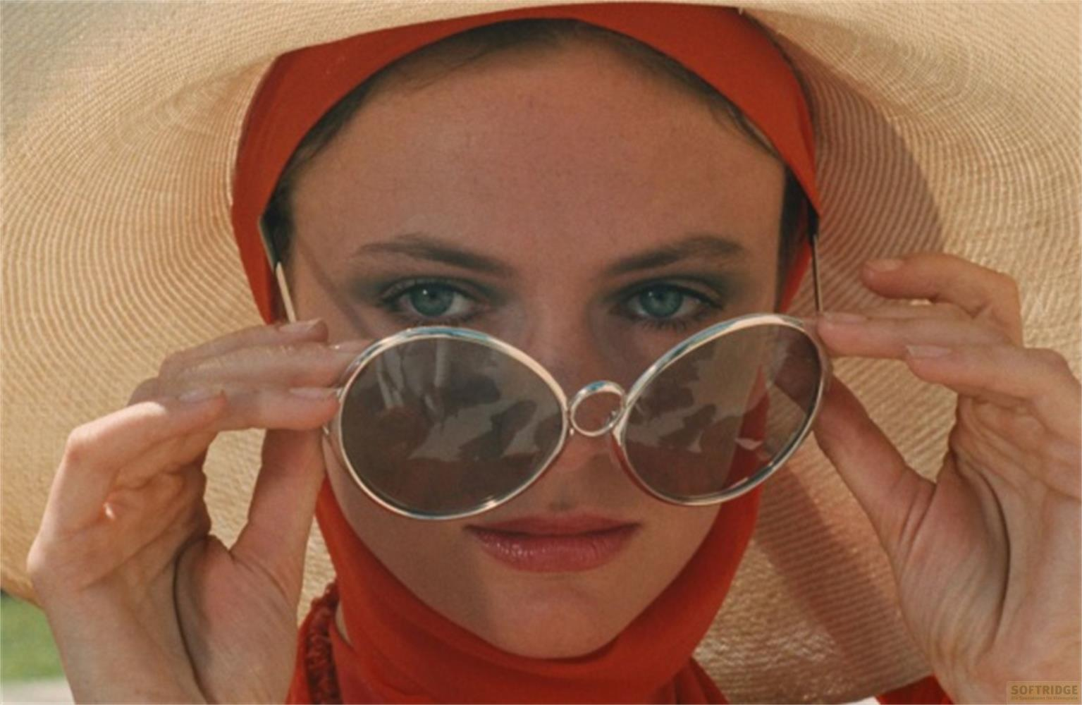 Frau mit Hut und Sonnenbrille, rot schimmerndes Tuch.