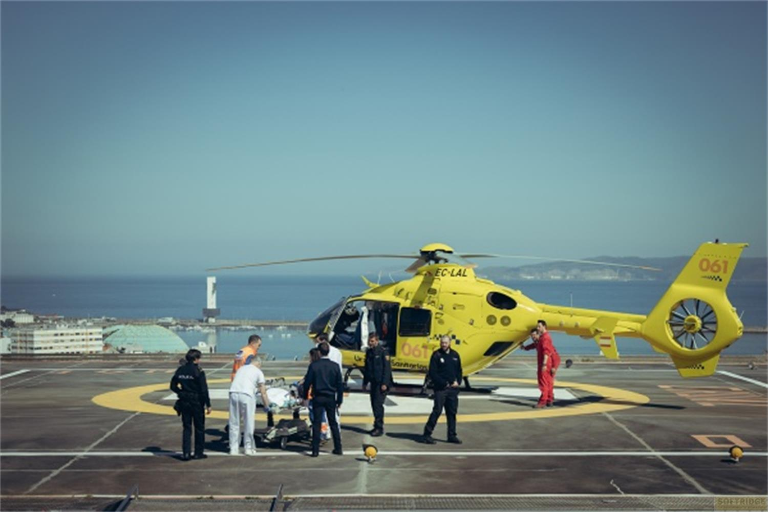 Un elicottero di soccorso giallo su un eliporto con un team che prepara una barella.
