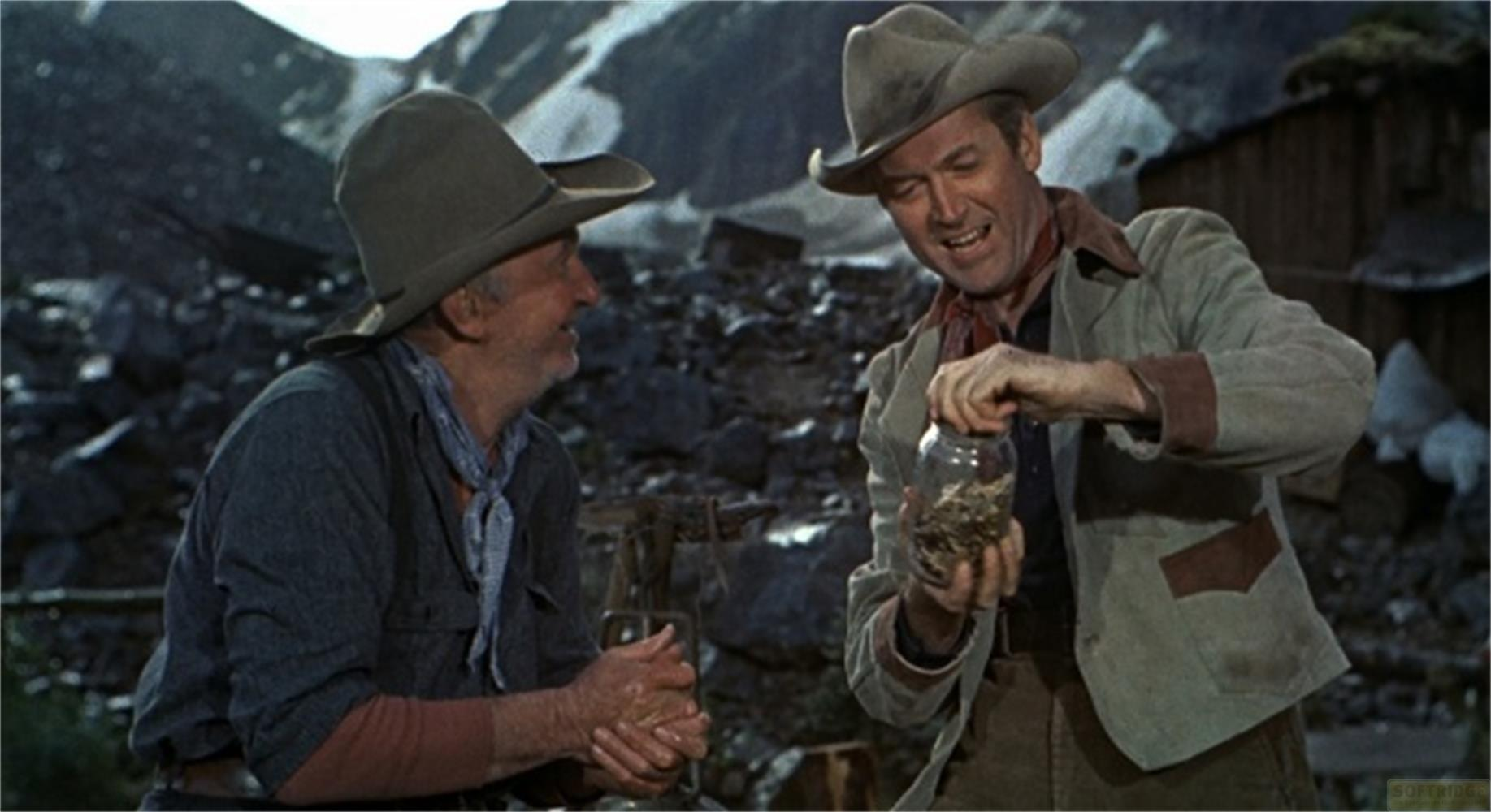 Due uomini con cappelli da cowboy su montagna rocciosa. Uno tiene un barattolo.