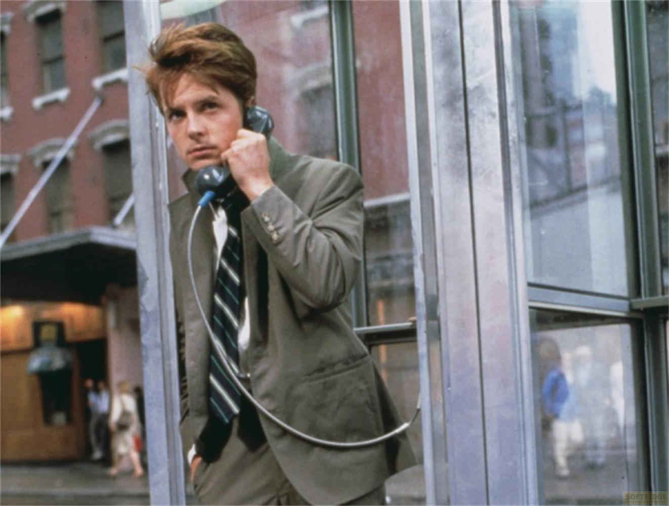 Un homme en costume parle au téléphone dans une cabine. Bâtiments flous à l'arrière-plan.