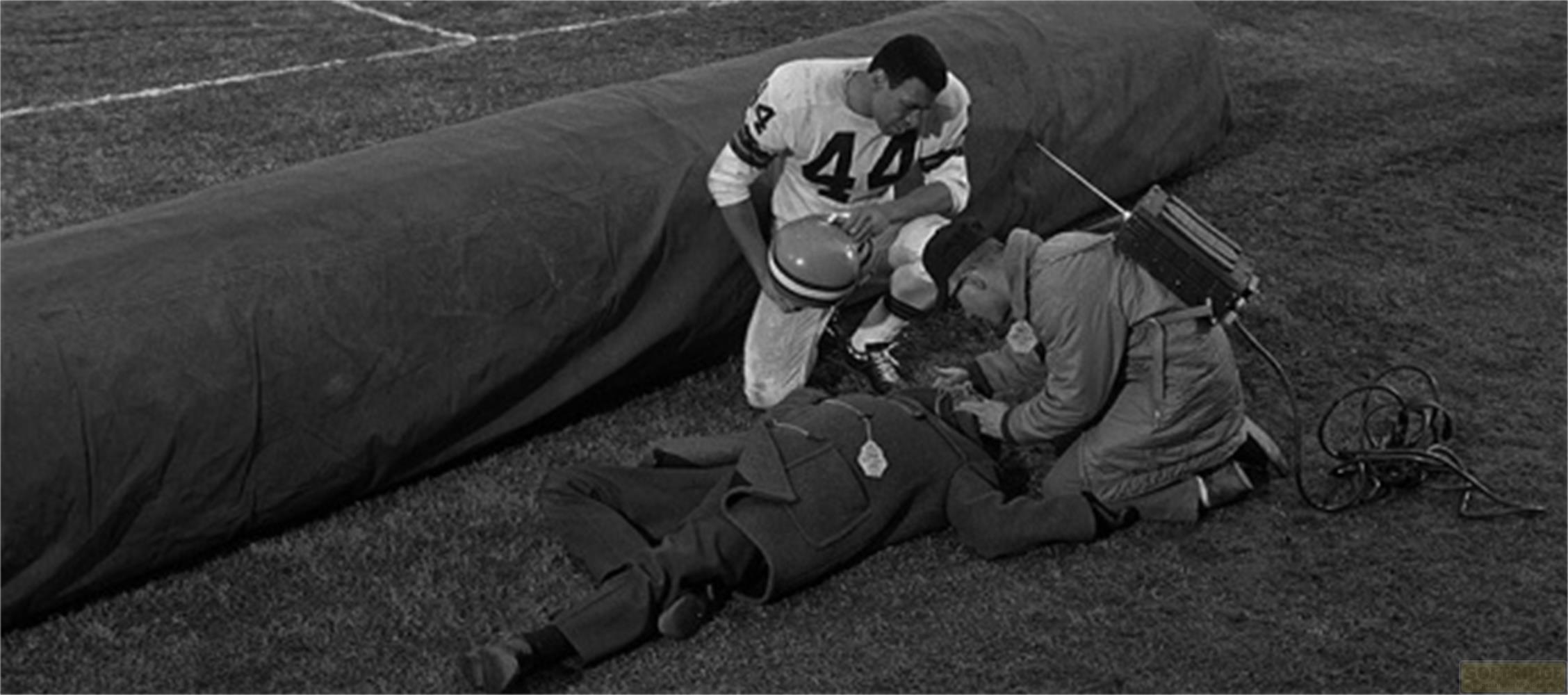 Giocatore di football guarda uomo ferito in campo con attrezzatura medica.
