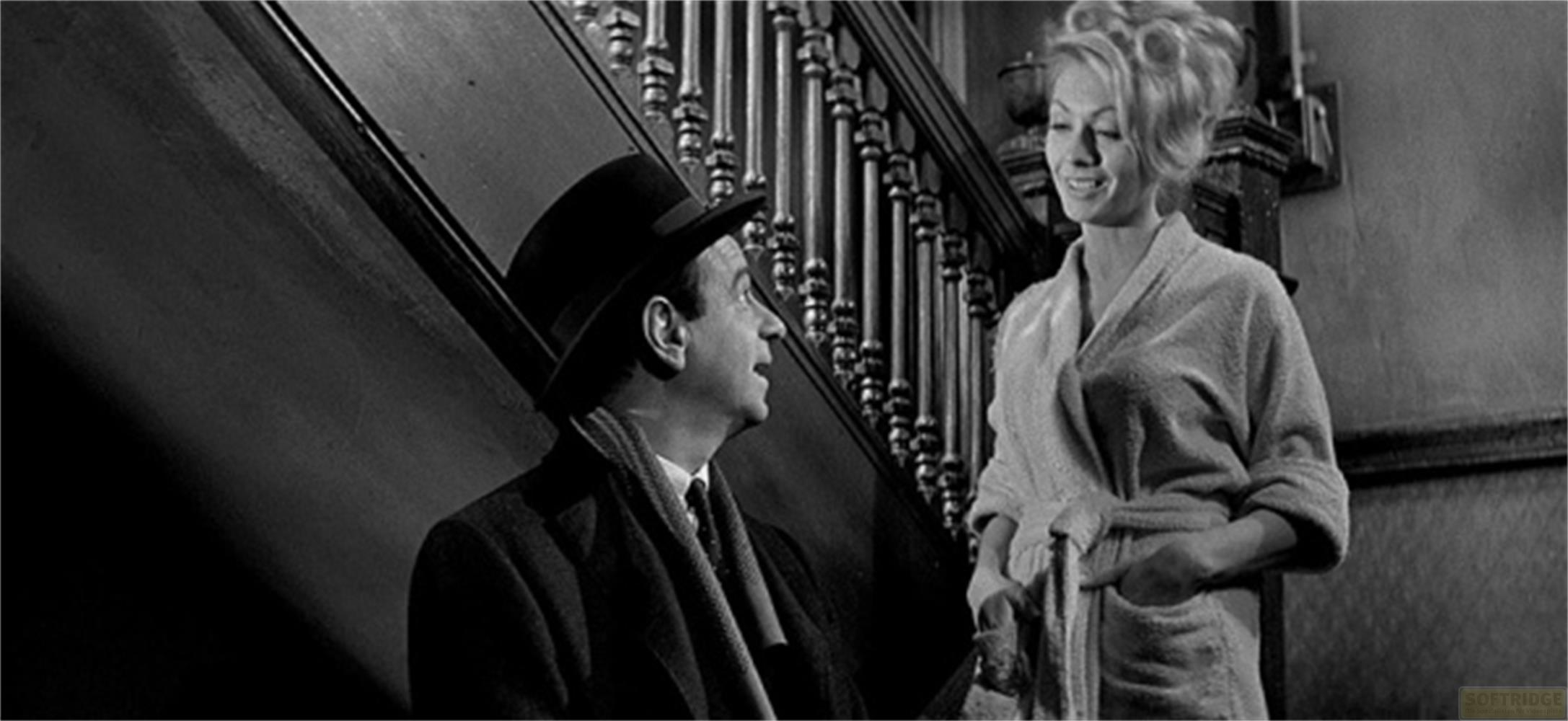 Uomo con cappello e sciarpa parla con donna in vestaglia sulle scale.