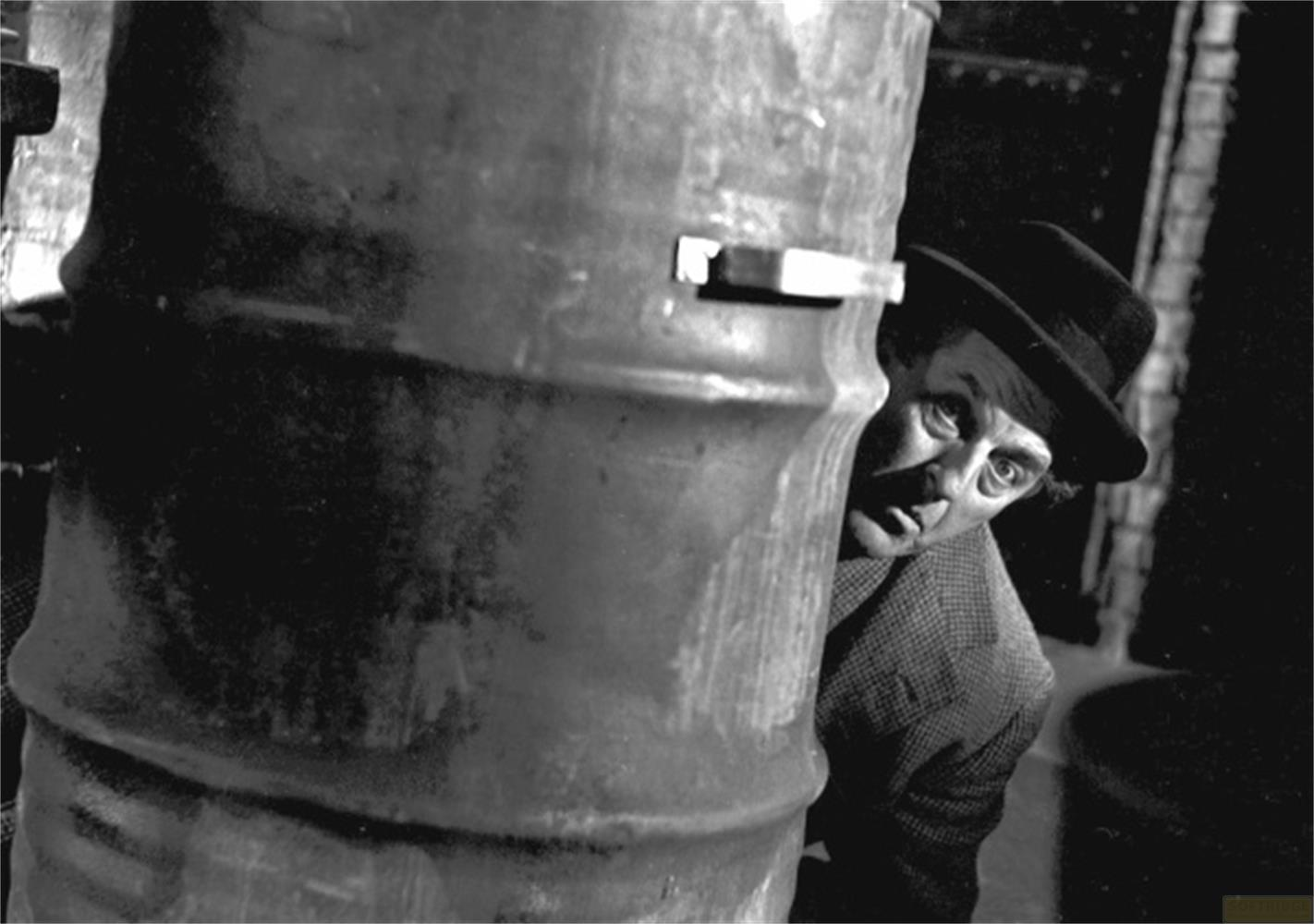 Un uomo con un cappello sbircia da dietro un barile.