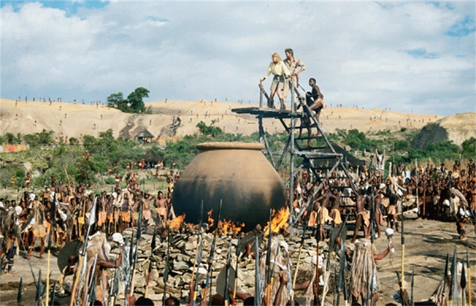 Un grand groupe de personnes en tenue traditionnelle se tient autour d'une marmite géante sur un feu.