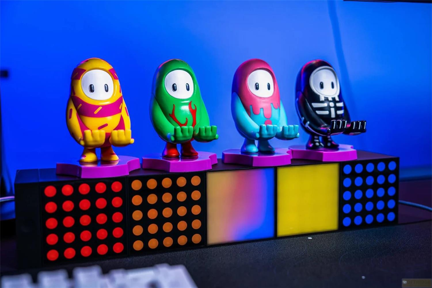 Quattro figure di Fall Guys su un piedistallo luminoso davanti a uno sfondo blu.