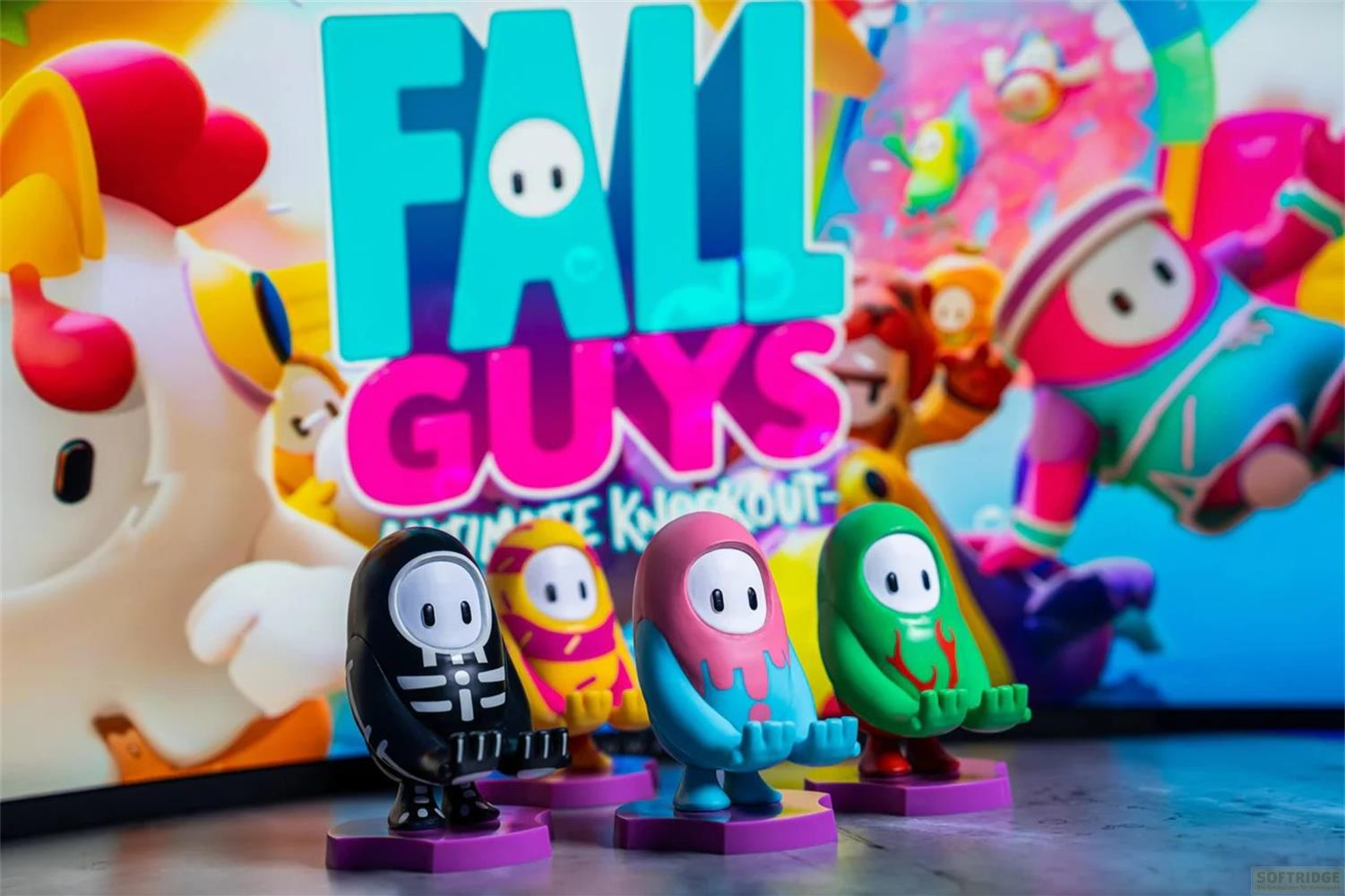Quattro figure di Fall Guys: nere, gialle, rosa e verdi, davanti al logo del gioco.