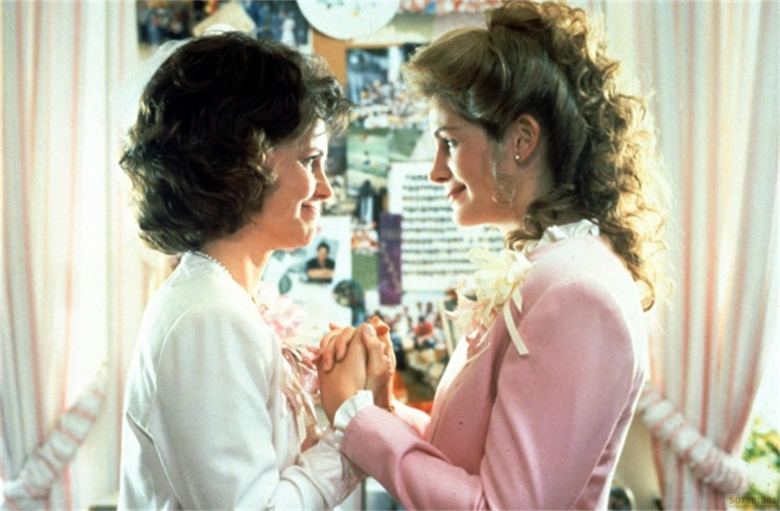 Due donne in abiti rosa si tengono per mano. Si guardano.
