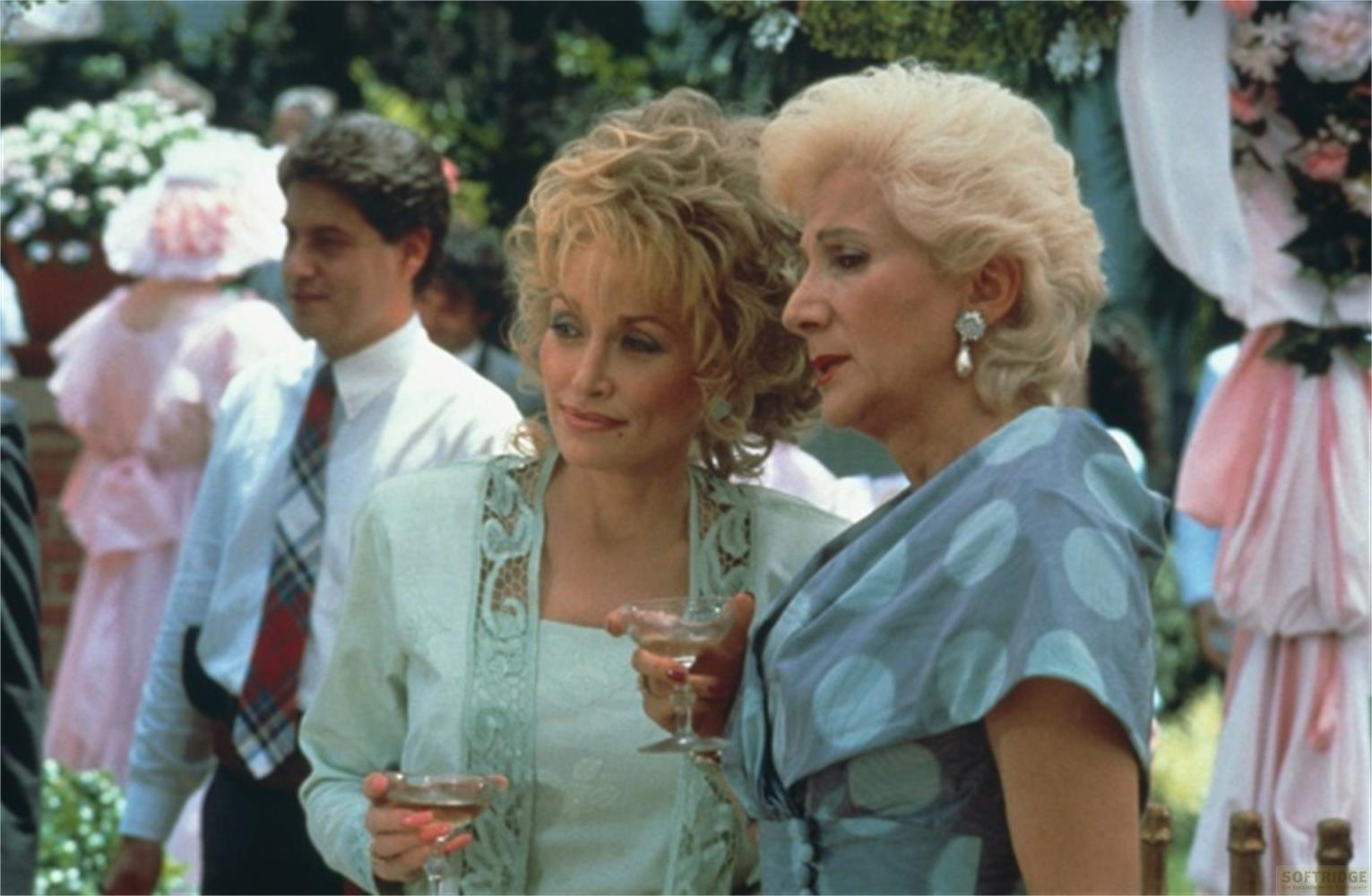 Due donne tengono bicchieri, con una scena di matrimonio sullo sfondo.