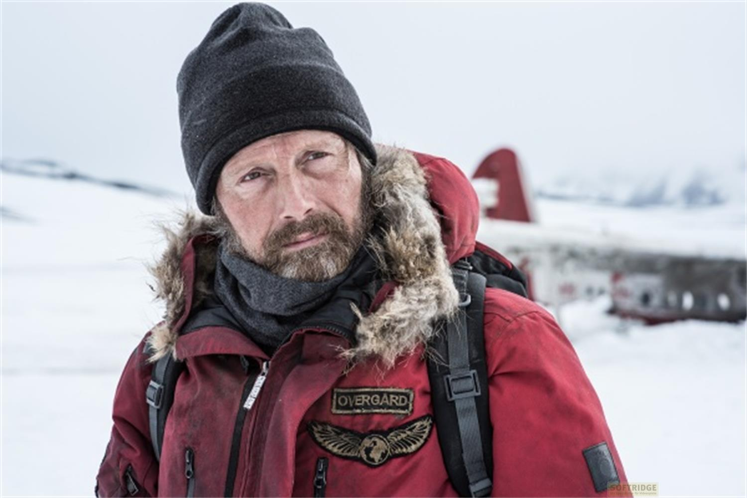 Uomo in cappotto invernale rosso e berretto in paesaggio nevoso.