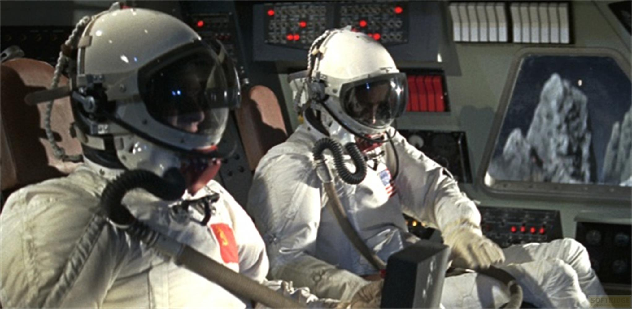 Deux astronautes en combinaisons blanches sont assis dans un cockpit. Une fenêtre montre un paysage rocheux.