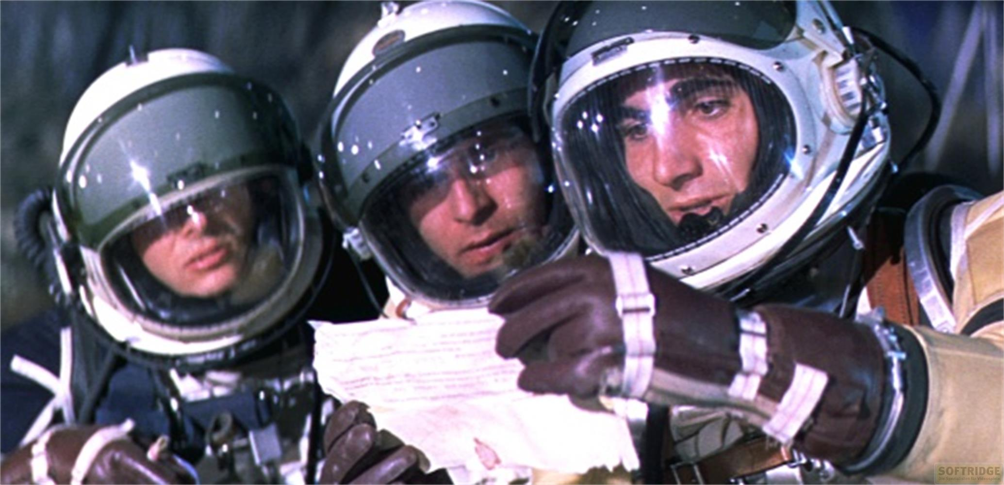 Trois astronautes casqués lisent un document à l'intérieur d'un vaisseau spatial.