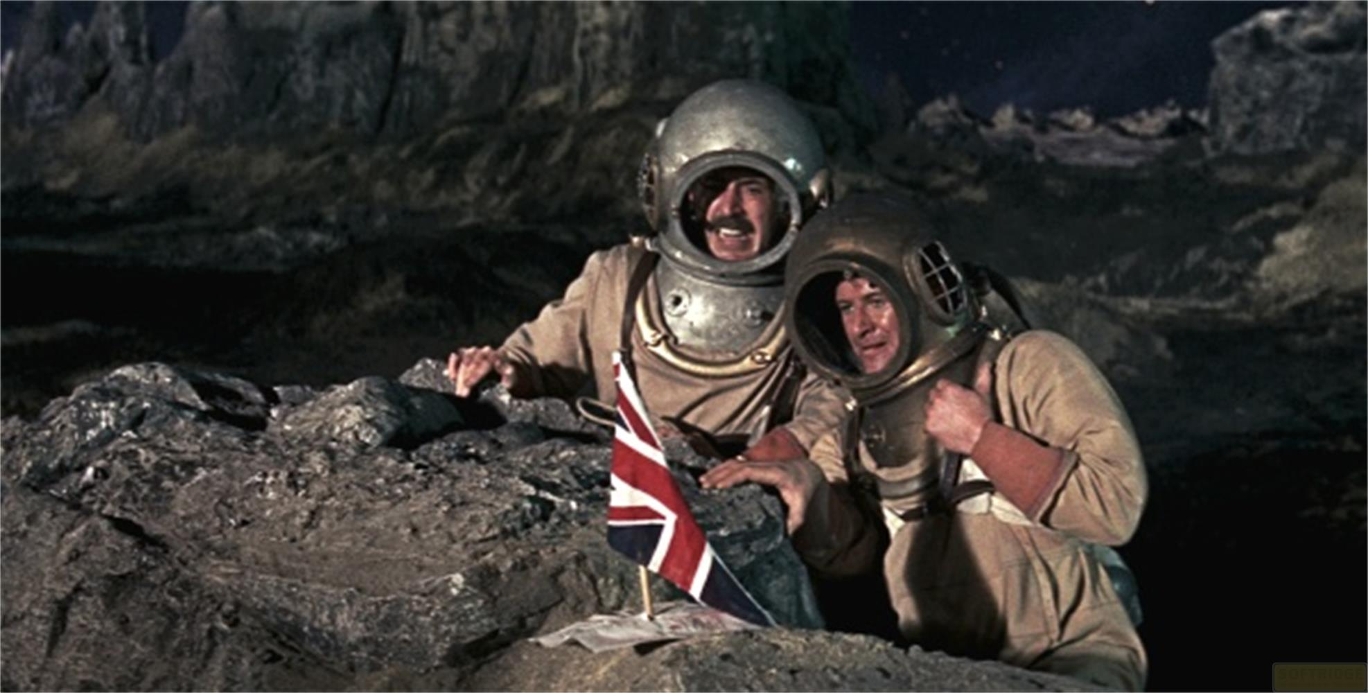 Deux astronautes casqués se tiennent sur un terrain rocheux avec un drapeau britannique.