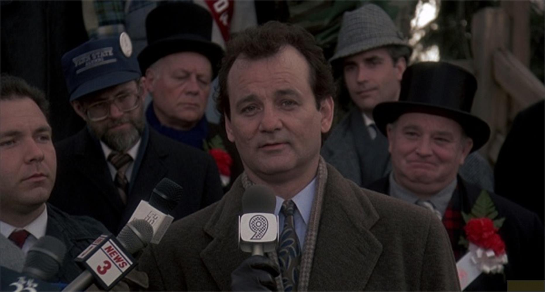 Bill Murray tiene microfoni davanti a una folla di uomini con cappelli.