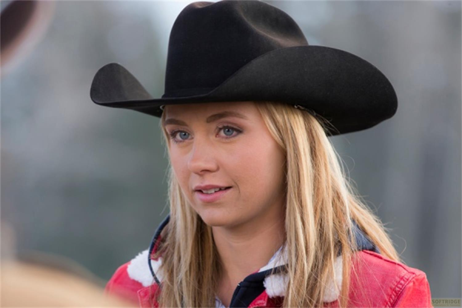 Una giovane donna bionda con cappello da cowboy nero e giacca rossa guarda di lato.