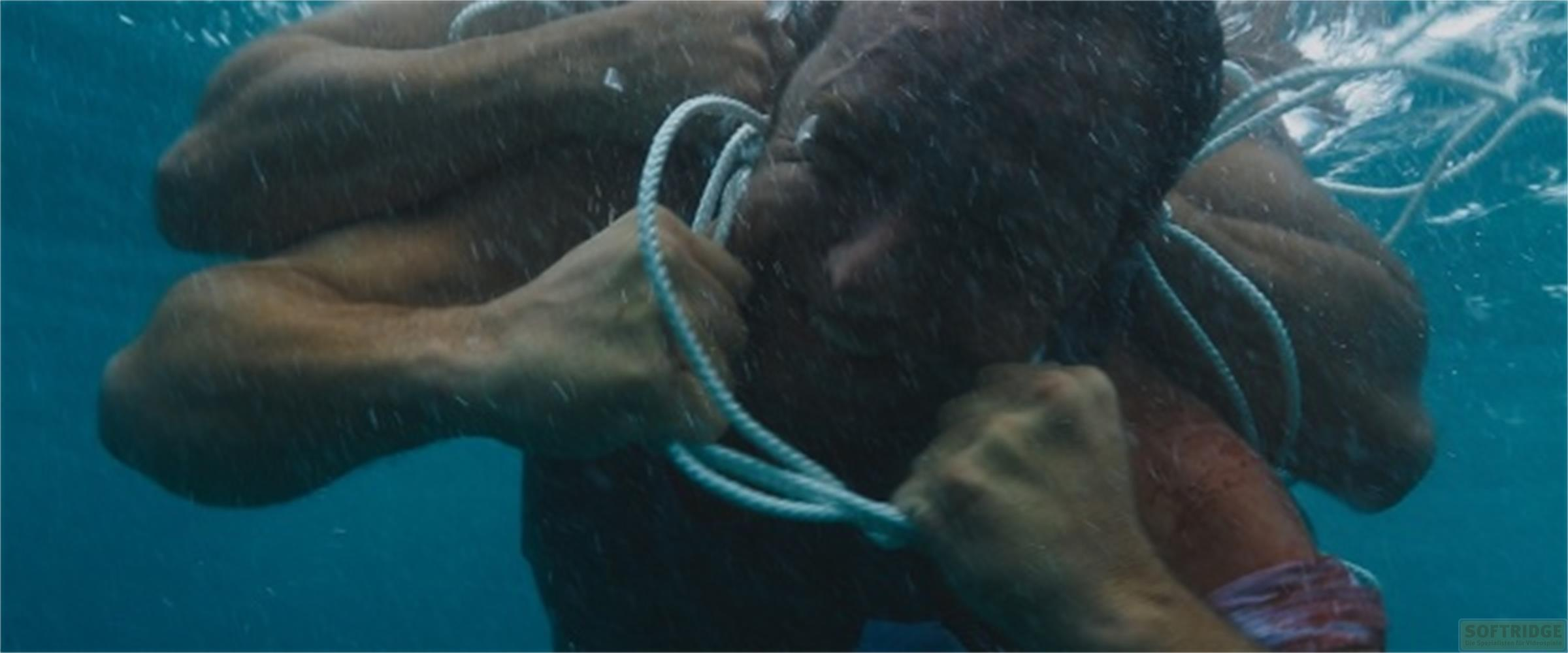 Un uomo si tira su con una corda sott'acqua, muscoli tesi.