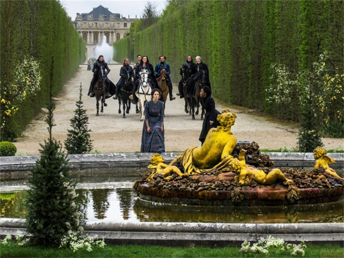 Un gruppo di cavalieri si avvicina a un palazzo attraverso un viale di siepi, con una statua dorata in primo piano.