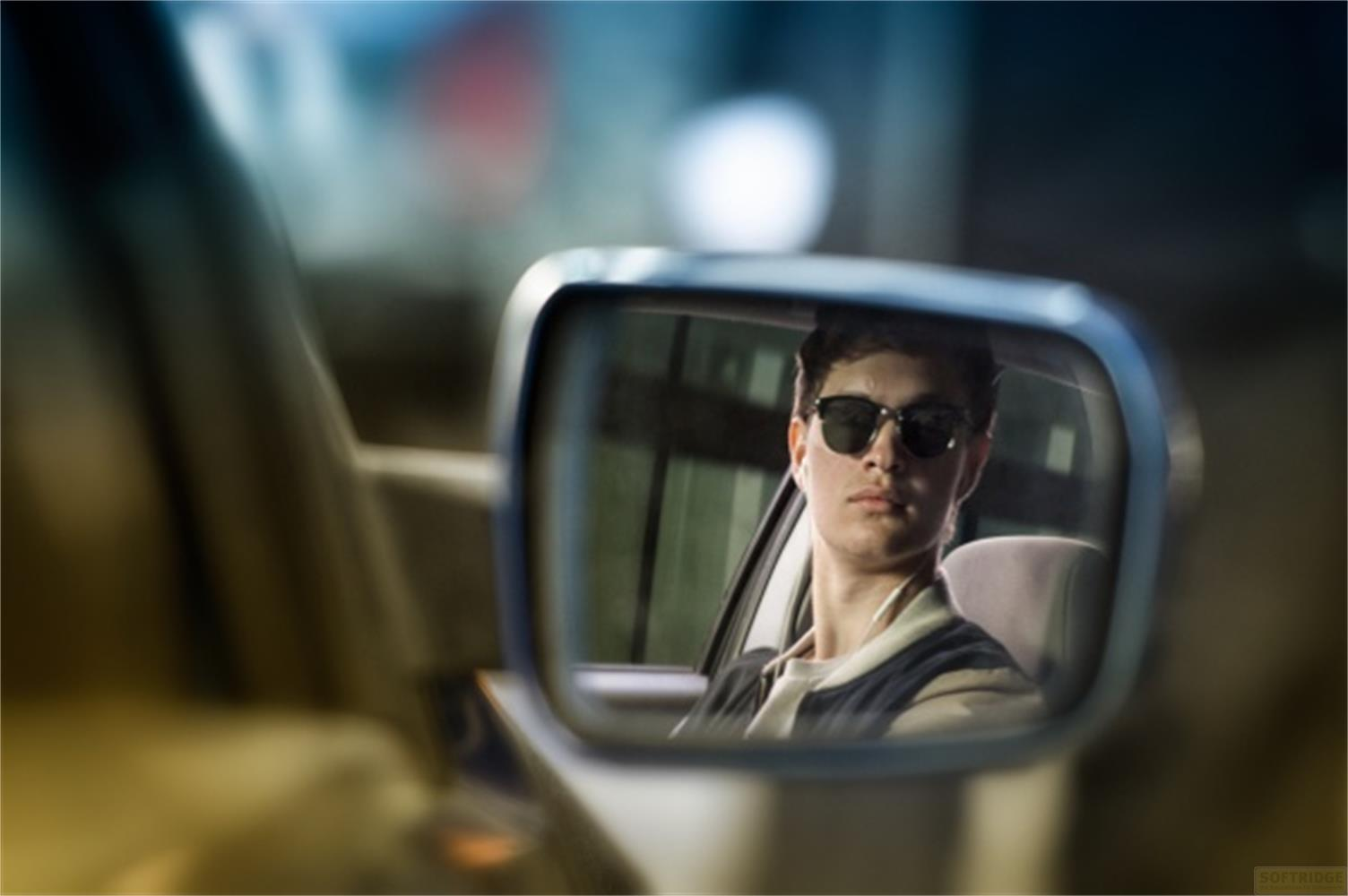 Un jeune homme portant des lunettes de soleil se reflète dans un rétroviseur.