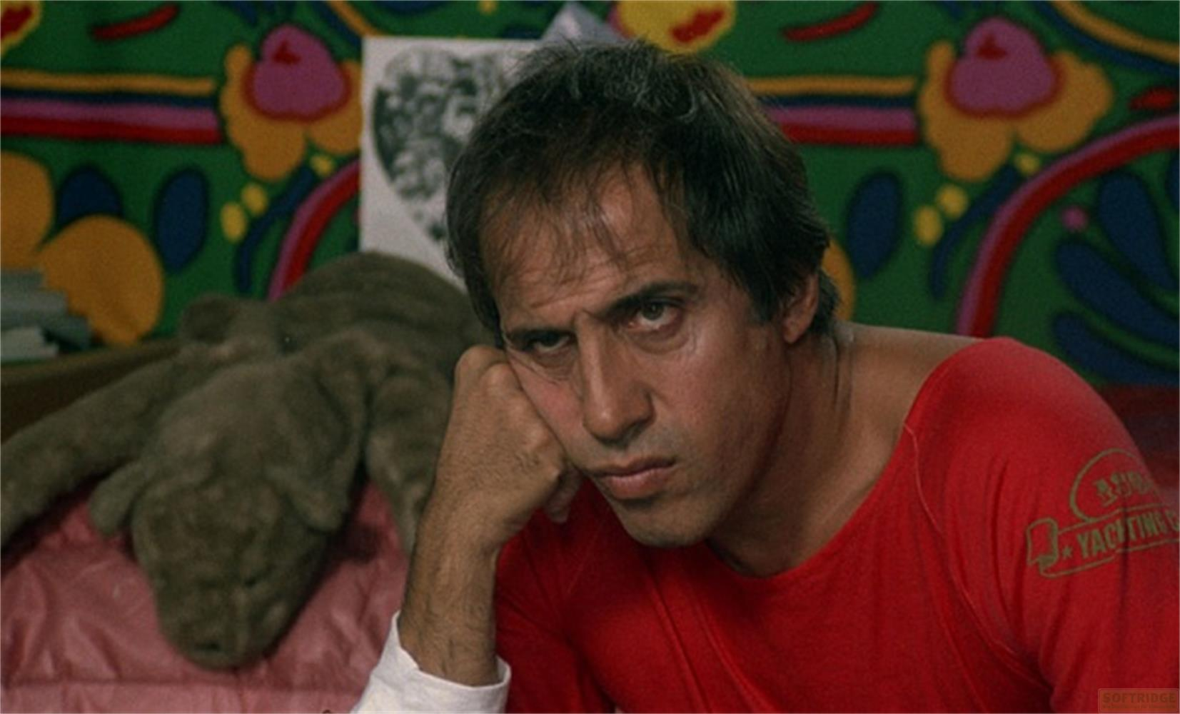 Uomo in camicia rossa appoggia la testa sulla mano. Un peluche è accanto.