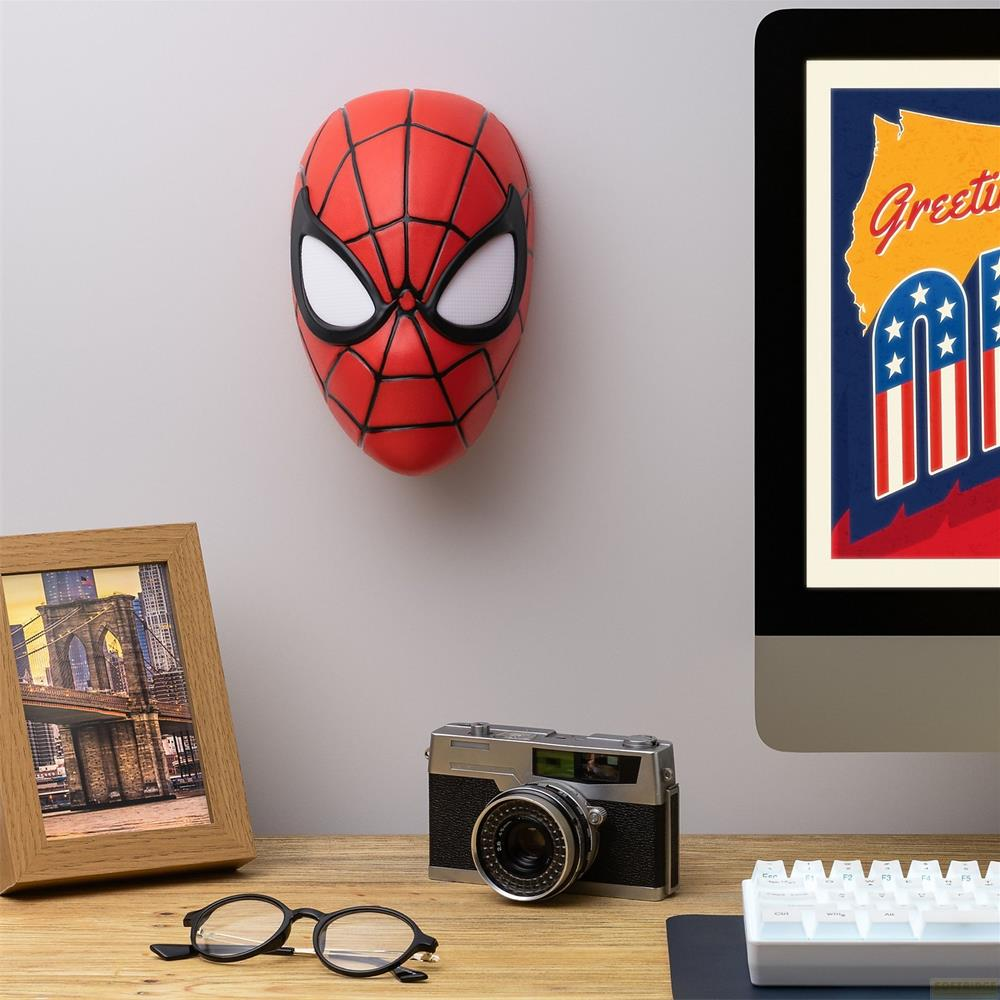 Maska Spidermana na ścianie, obok ramka na zdjęcie, aparat i okulary.