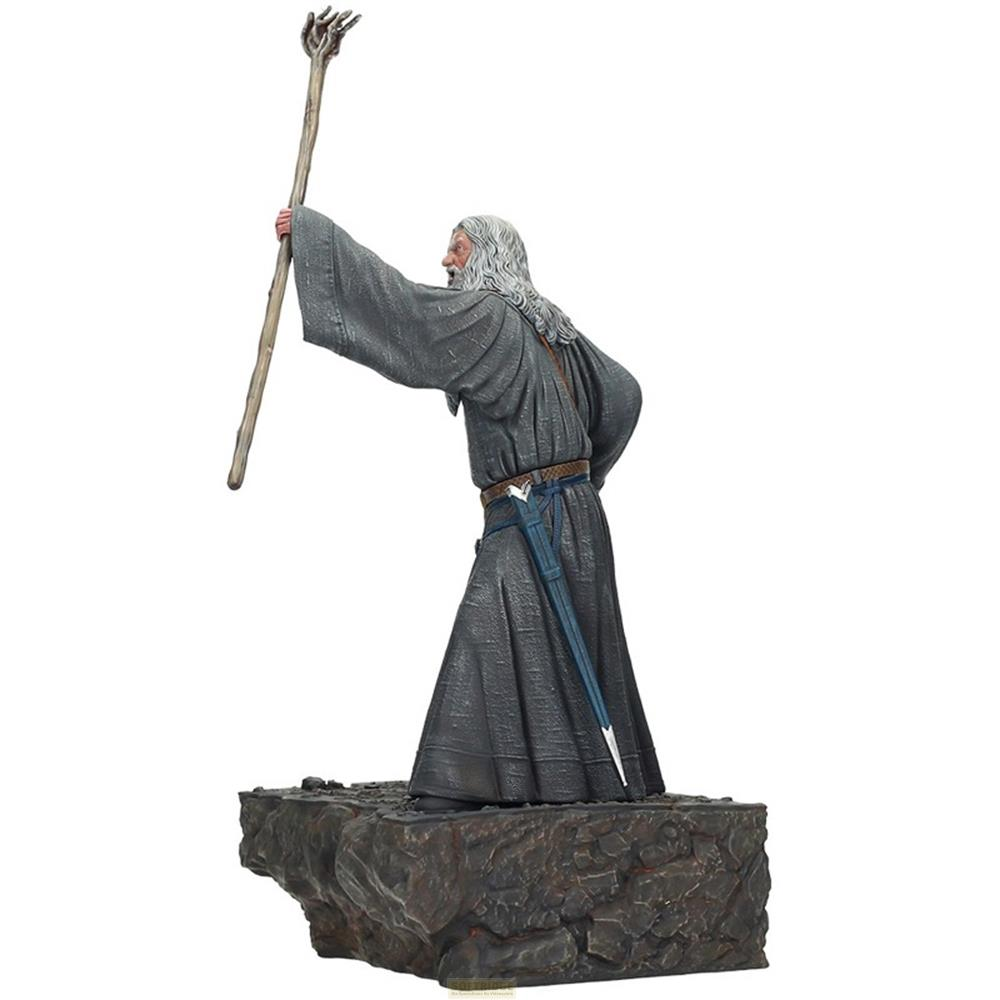 Gandalf con bastón y espada de pie sobre rocas.