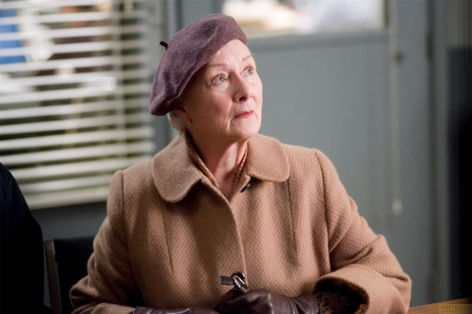 Femme âgée en manteau brun, foulard et béret regarde vers le haut.