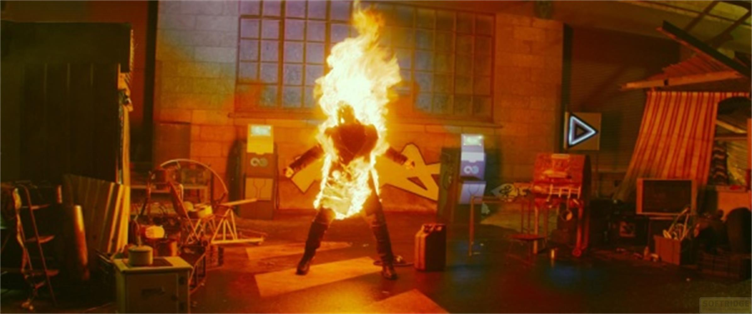 Un uomo avvolto dalle fiamme si erge tra cabinati arcade e detriti.