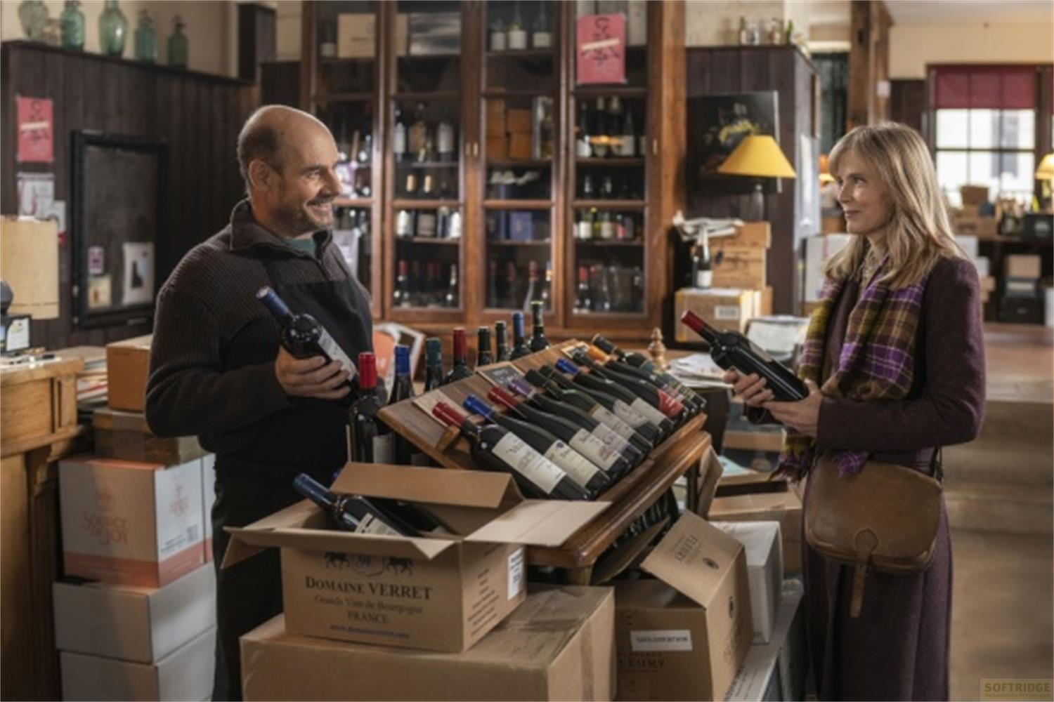 Un uomo e una donna in un negozio di vini, circondati da scatole e bottiglie. Tengono bottiglie.
