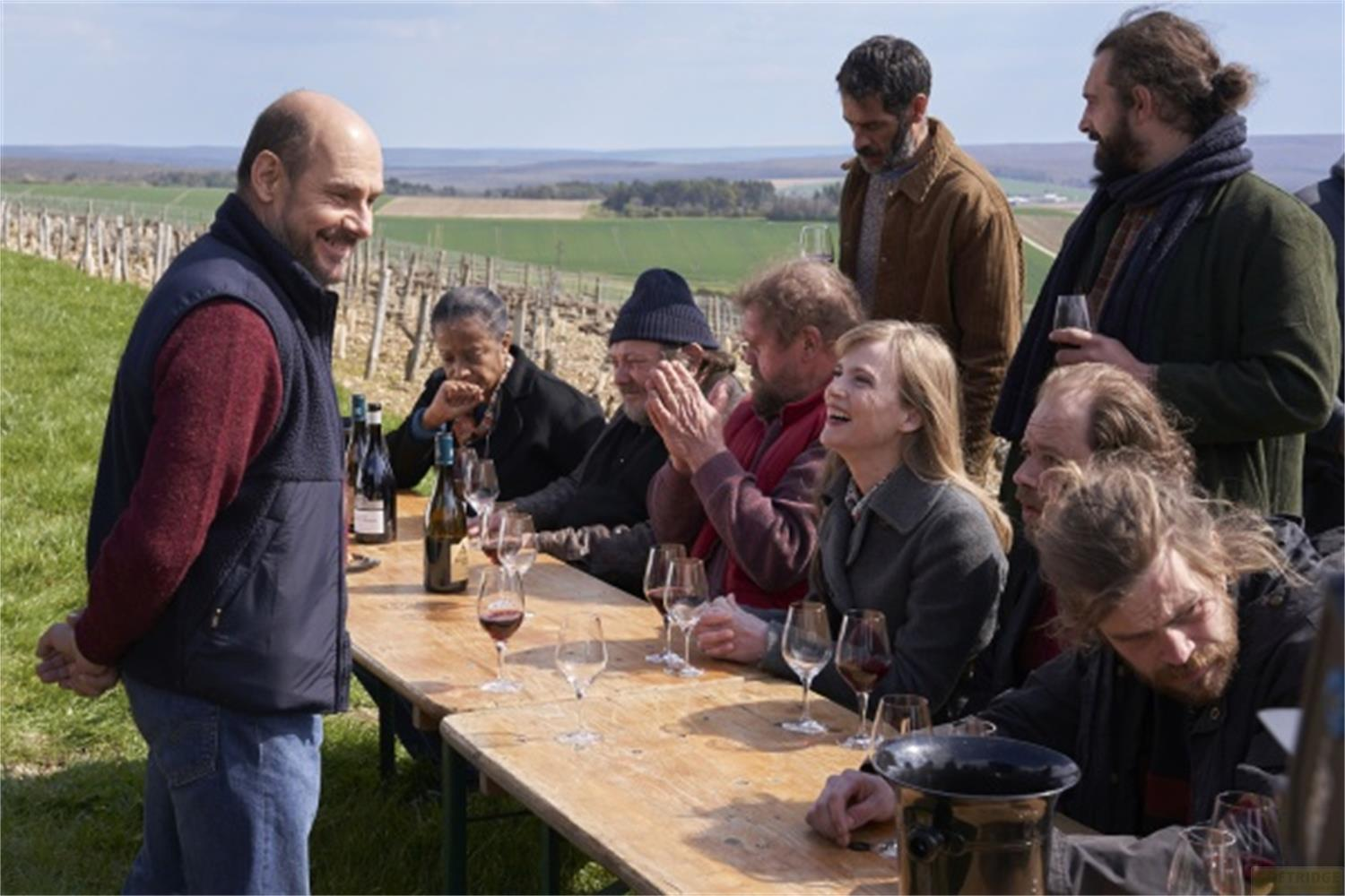 Un gruppo di persone siede a un tavolo di legno all'aperto con bottiglie di vino.