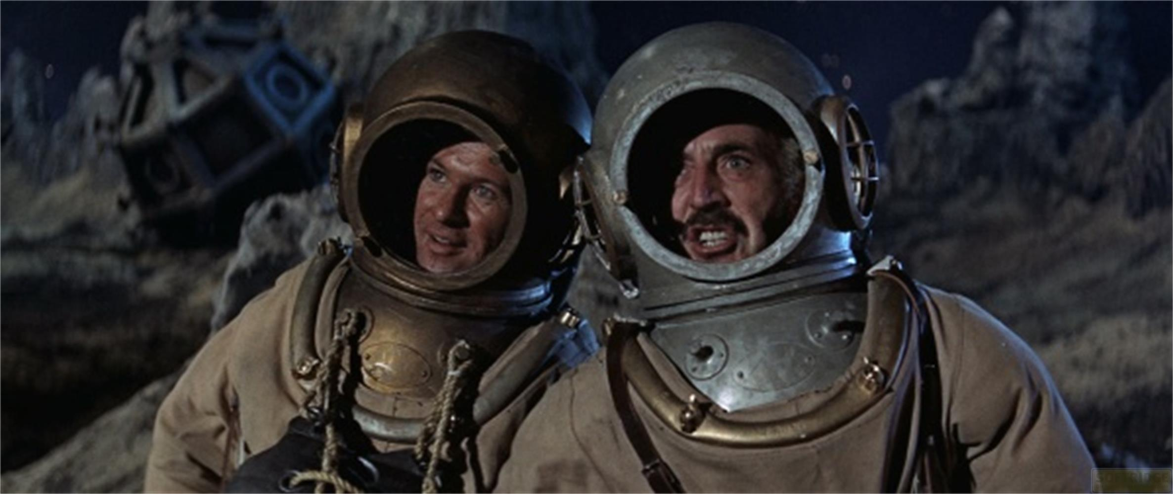 Deux plongeurs aux vieux casques regardent à droite. Des rochers à l'arrière.