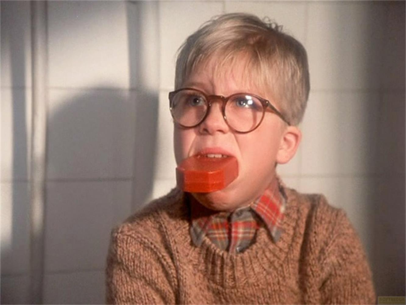 Un ragazzo con gli occhiali tiene il sapone in bocca, indossa un maglione.