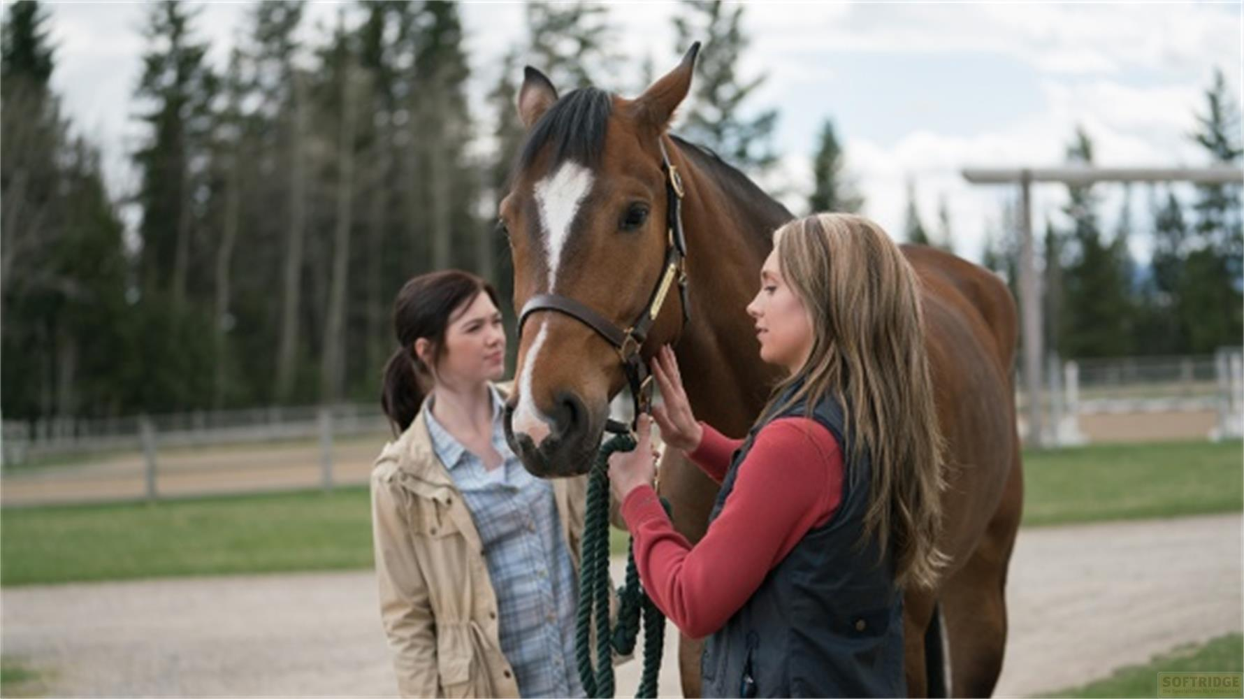 Due donne accanto a un cavallo marrone in un maneggio esterno.
