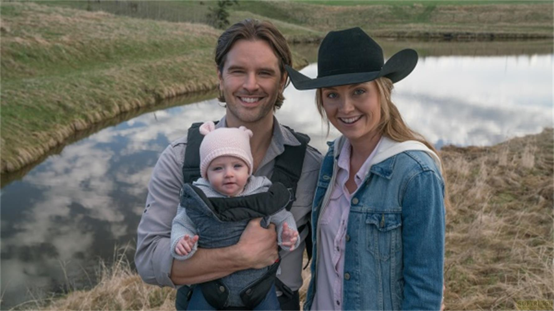 Un uomo con marsupio, un bambino e una donna con cappello vicino all'acqua.