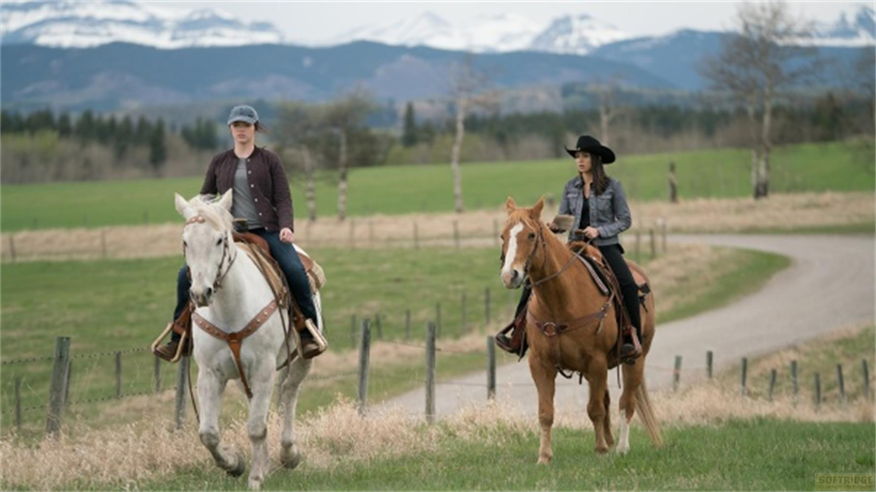 Due donne a cavallo cavalcano in un paesaggio rurale con montagne sullo sfondo.