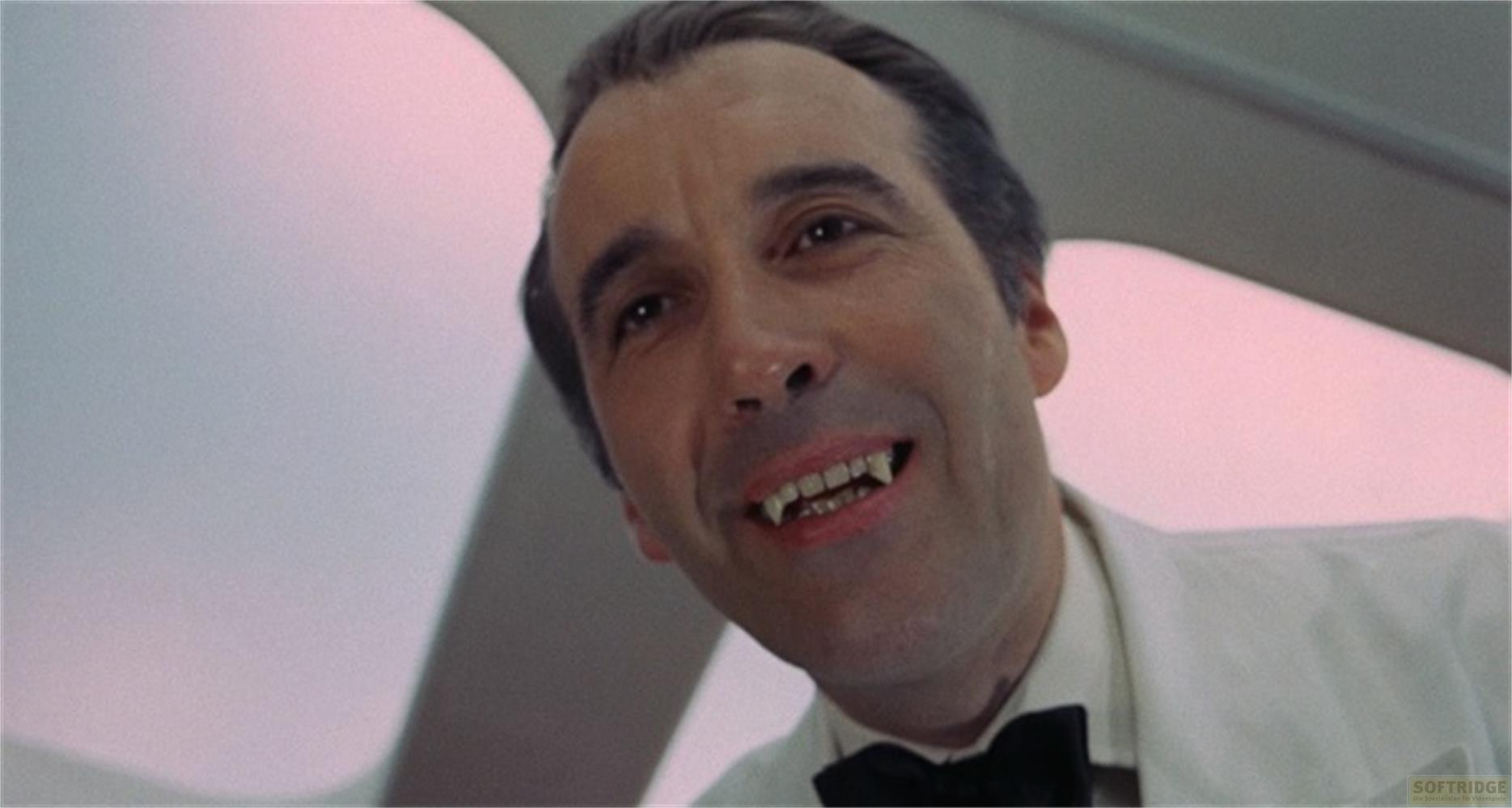 Un uomo in abito bianco con papillon nero indossa zanne da vampiro.