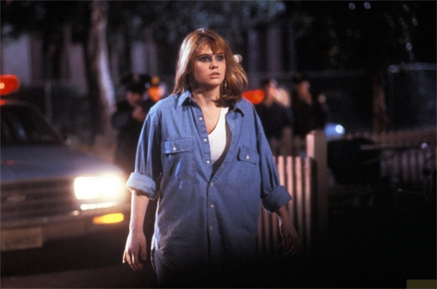 Una donna in camicia blu e maglietta bianca sta fuori di notte.