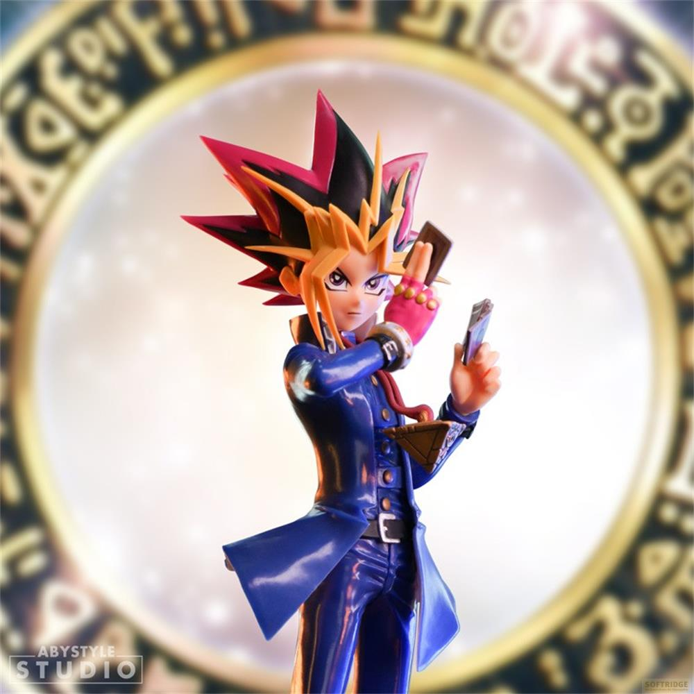Yugi Muto Figur in blauer Uniform hält Spielkarten vor rundem goldenem Kreis.
