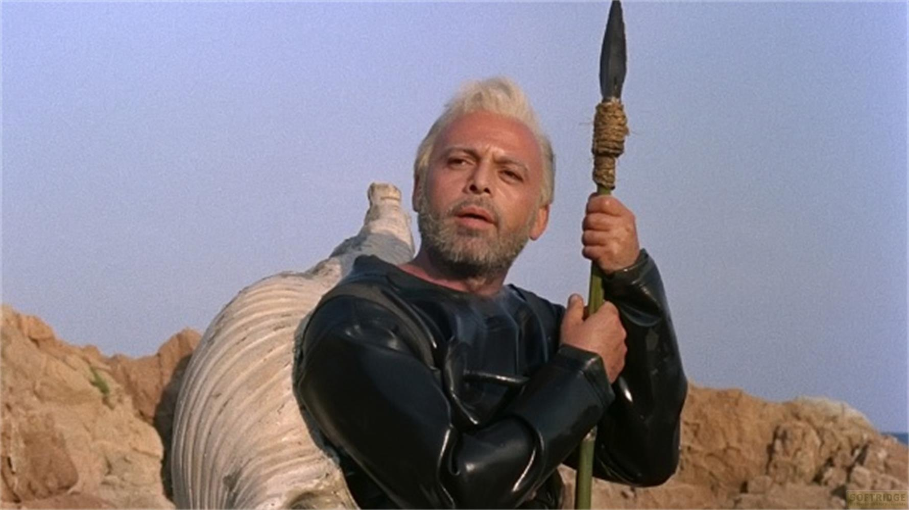 Un homme aux cheveux blonds et à la barbe tient une lance, vêtu de cuir noir.